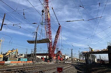 Ein Schwerlast-Raupenkran hebt ein massives Brückensegment der Hauptbahnhofbrücke in Hanau aus © KREBS+KIEFER