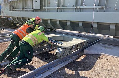 Fachkräfte manövrieren das Fahrwerk unter den Transformator, um den Richtungswechsel für den Quer- und Längsverzug vorzubereiten 