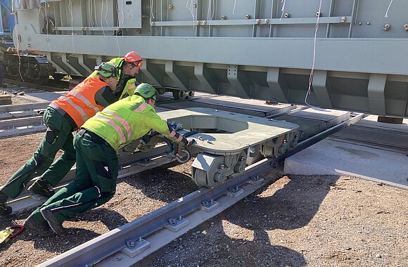 Fachkräfte manövrieren das Fahrwerk unter den Transformator, um den Richtungswechsel für den Quer- und Längsverzug vorzubereiten 