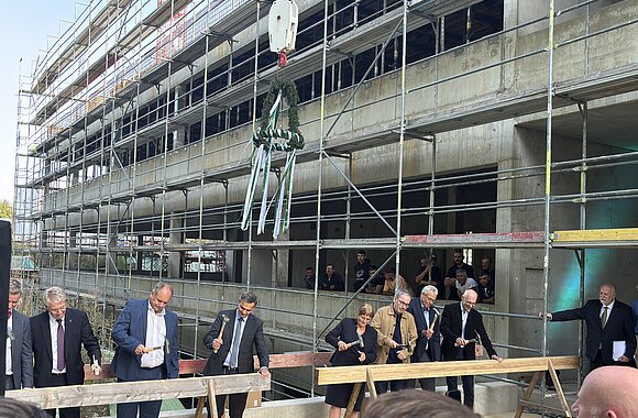Traditioneller Nageleinschlag beim Richtfest mit Richtkranz. Von links: Dr.-Ing. E. h. Thomas Reiter, Abteilungsleiter für Raumfahrt und Sicherheit im Bundesministerium für Forschung, Technologie und Raumfahrt; Dirk Hilbert, Oberbürgermeister der Landeshauptstadt Dresden; Falk Reinhardt, Technischer Geschäftsführer des Staatsbetriebs Sächsisches Immobilien- und Baumanagement; Juliane Schmidt, Kaufmännische Direktorin des IFW Dresden; Jan Gerken, Kanzler der TU Dresden; Prof. Dr. Bernd Büchner, Wissenschaftlicher Direktor des IFW Dresden, und Prof. Dr. Matthias Vojta, Sprecher des Exzellenzclusters ctd.qmat.